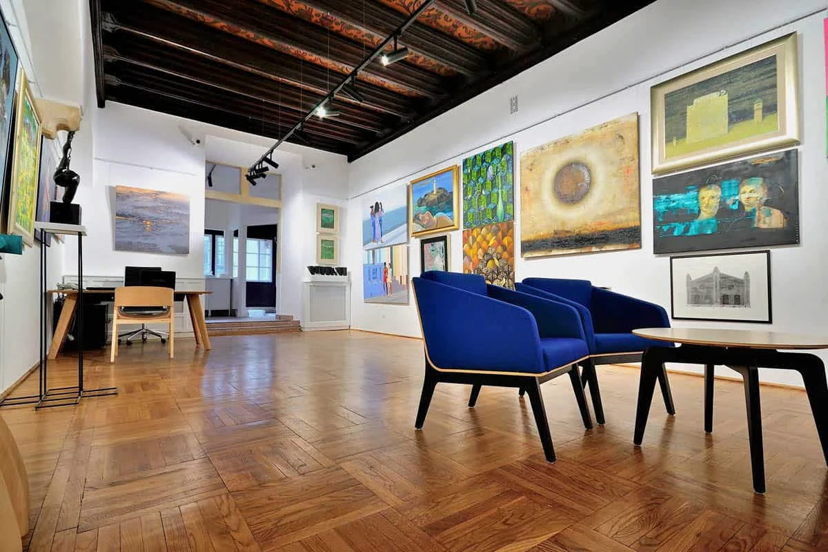 Exhibition room at Kersten Gallery with a timber ceiling, paintings on the walls and armchairs for visitors